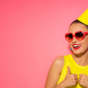 A young woman in a yellow dresw and matching party hat give a thumbs up