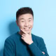 Portrait of a young Asian man, smiling with a hand on his chin.