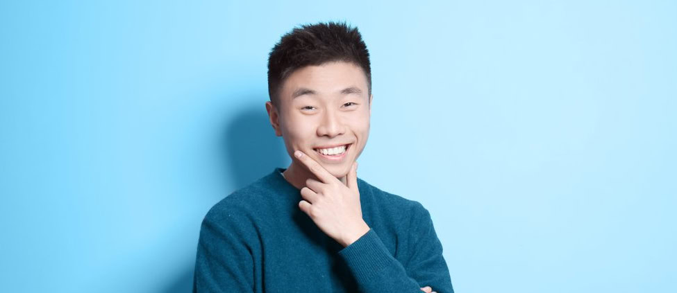 Portrait of a young Asian man, smiling with a hand on his chin.
