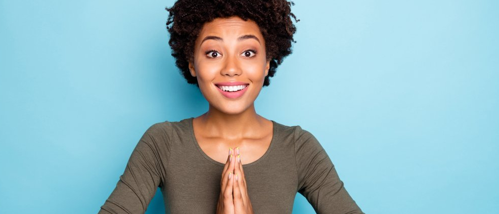 Photo of a cheerful young woman pressing her hands together in the prayer position