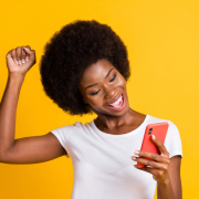 Photo of a young man, holding her phone, and raising her fist in victory