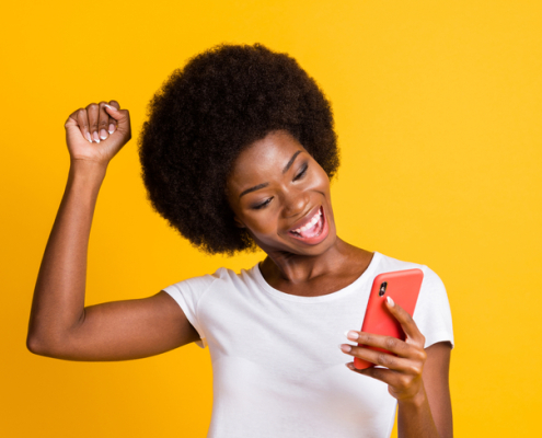 Photo of a young man, holding her phone, and raising her fist in victory